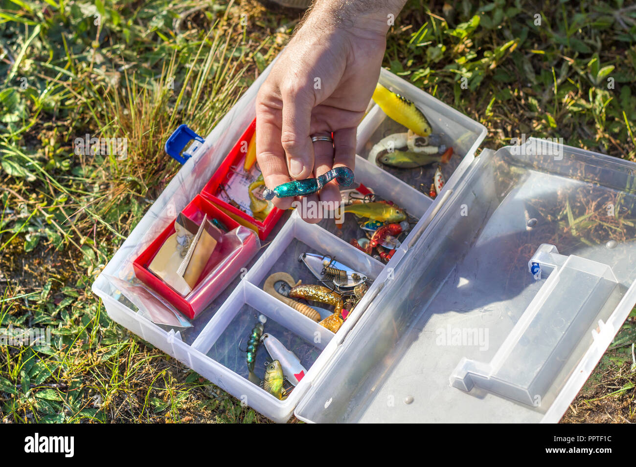 An angler's rod chooses a spinning bait from the box. The fisherman chooses a rubber bait from the box. Stock Photo