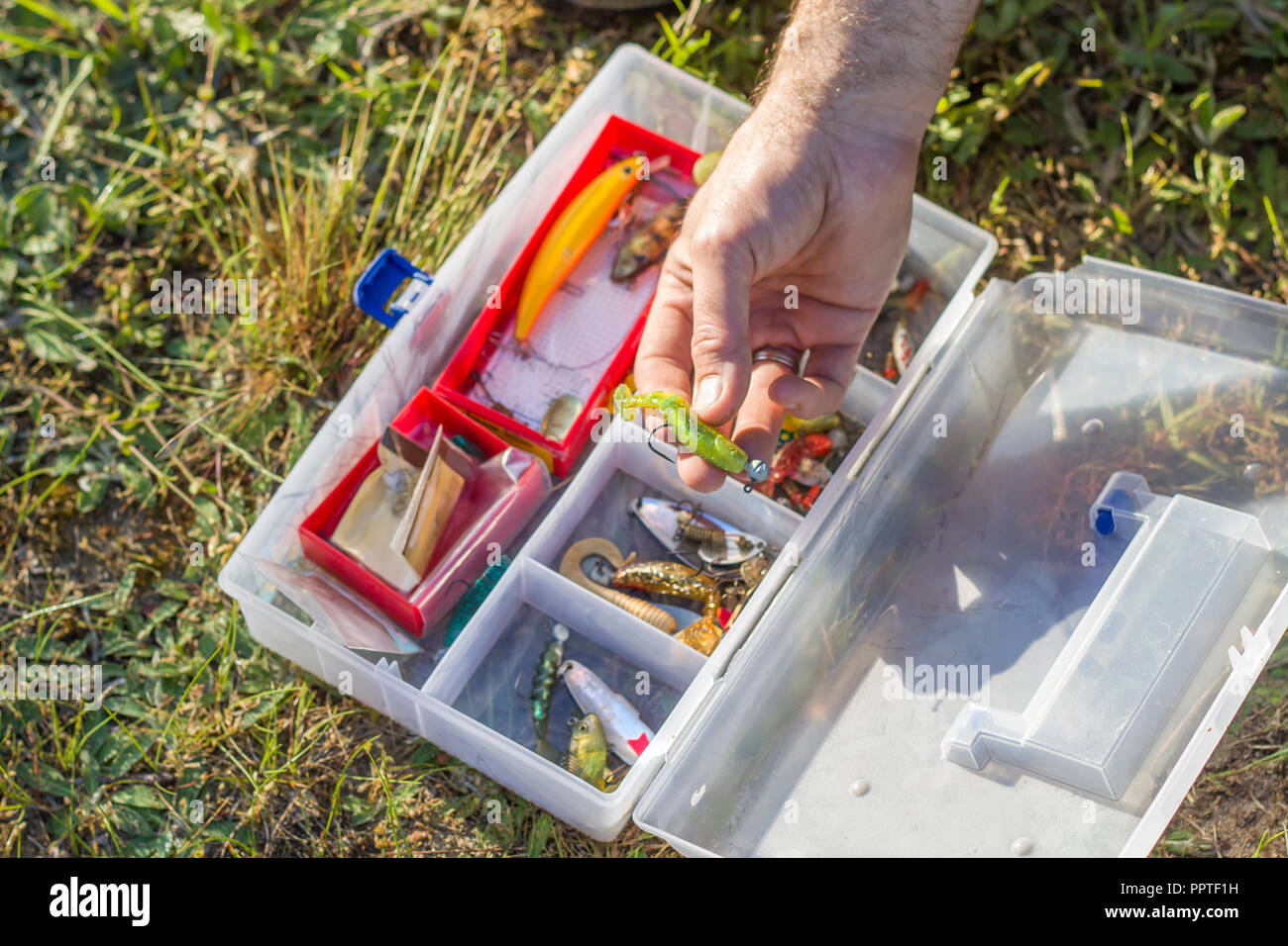 An angler's rod chooses a spinning bait from the box. The fisherman chooses a rubber bait from the box. Stock Photo
