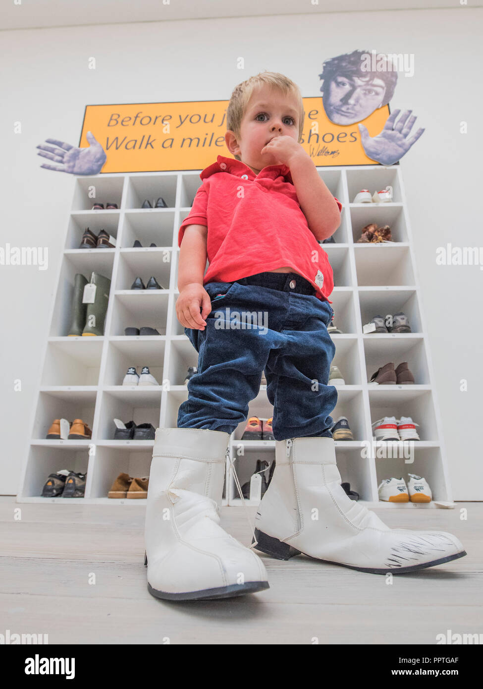 London, UK. 27th Sep 2018. Emlyn Simmonds (age 2.5) tries the shoes for size - Bedwyr Williams' Walk A Mile In My Shoes, a display case with 45 pairs of his own size 13 shoes. He invites the audience to share in his own 'problems of podietry ' by trying them on - Black Mirror the new exhibition at the Saatchi Gallery about art’s role in social satire - featuring the work of 26 contemporary artists. It runs from 28 Sept 18 to 13 Jan 19. Credit: Guy Bell/Alamy Live News Stock Photo