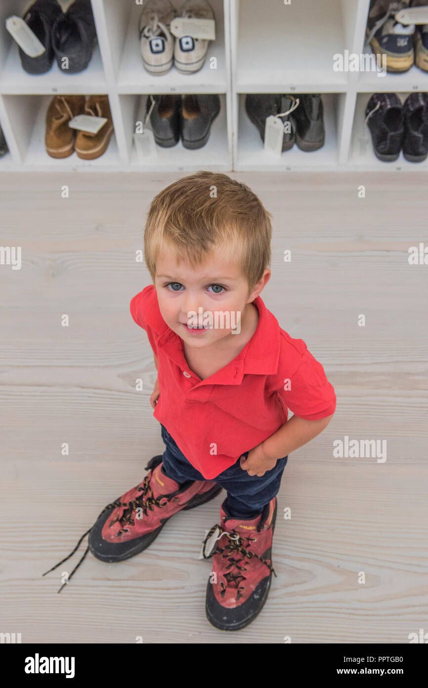 London, UK. 27th Sep 2018. Emlyn Simmonds (age 2.5) tries the shoes for size - Bedwyr Williams' Walk A Mile In My Shoes, a display case with 45 pairs of his own size 13 shoes. He invites the audience to share in his own 'problems of podietry ' by trying them on - Black Mirror the new exhibition at the Saatchi Gallery about art’s role in social satire - featuring the work of 26 contemporary artists. It runs from 28 Sept 18 to 13 Jan 19. Credit: Guy Bell/Alamy Live News Stock Photo