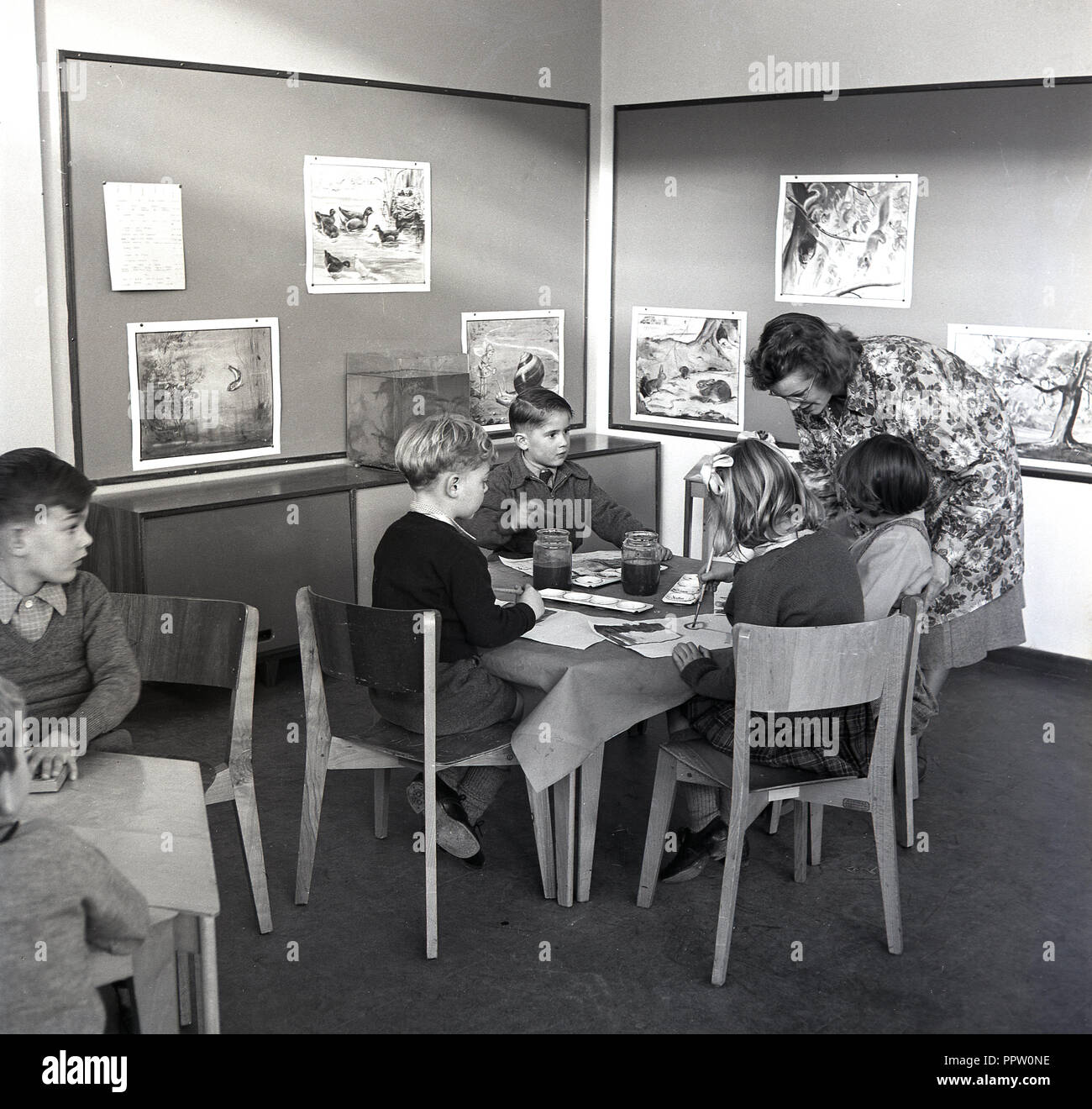 1960s, historical, female teacher with primary school children sitting at tables in an art class painting pictures with watercolours, England, UK. Stock Photo