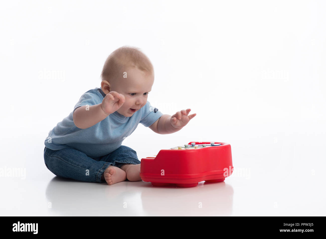 A seven month old baby boy playing with a toy piano. Shot in the studio on a white, seamless backdrop. Stock Photo