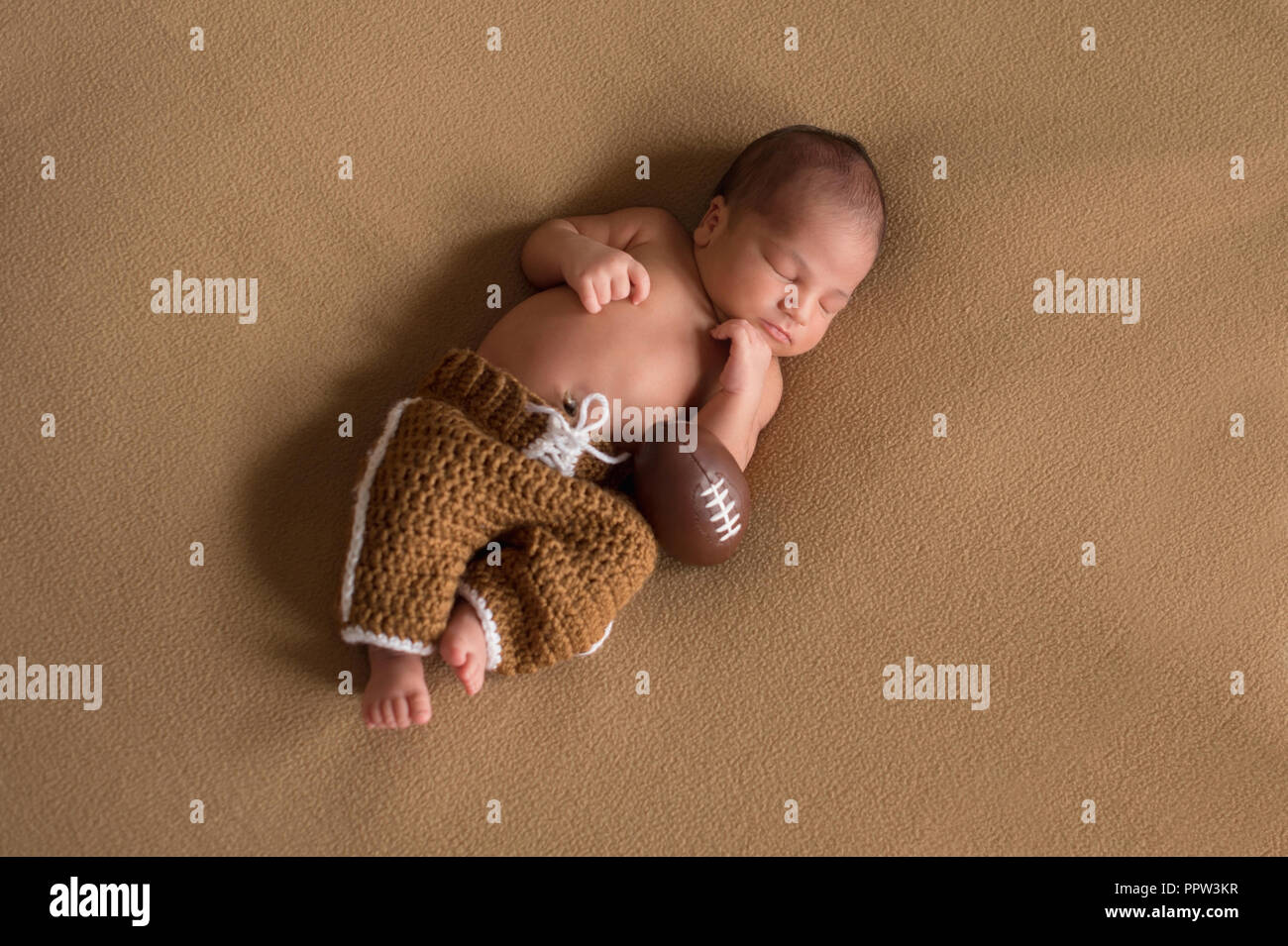 A sleeping, nine day old newborn baby boy wearing crocheted football uniform pants. Stock Photo
