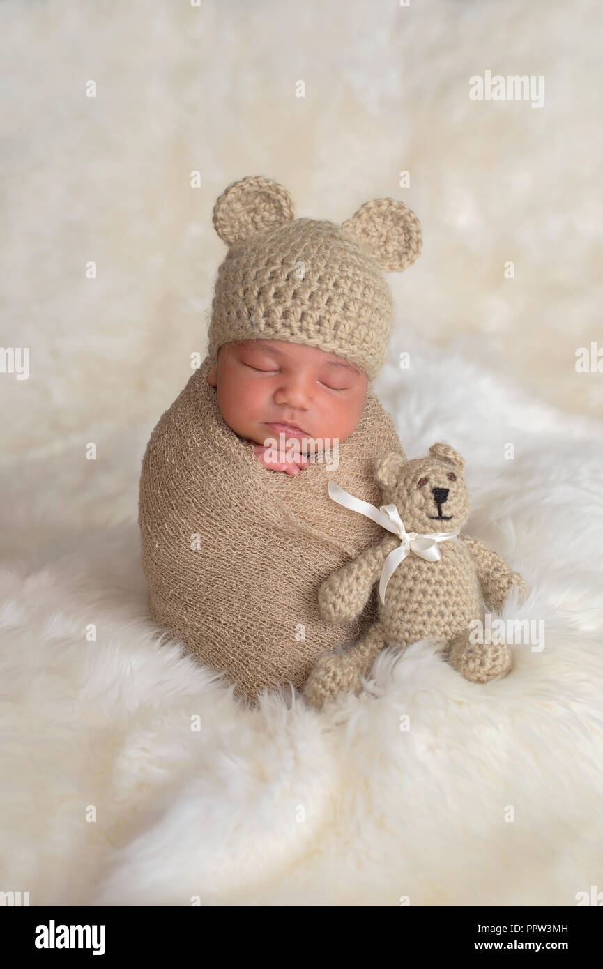 Nine day old newborn baby boy wearing a tan, crocheted bear hat. He is sleeping upright while swaddled with a stretch wrap. Stock Photo
