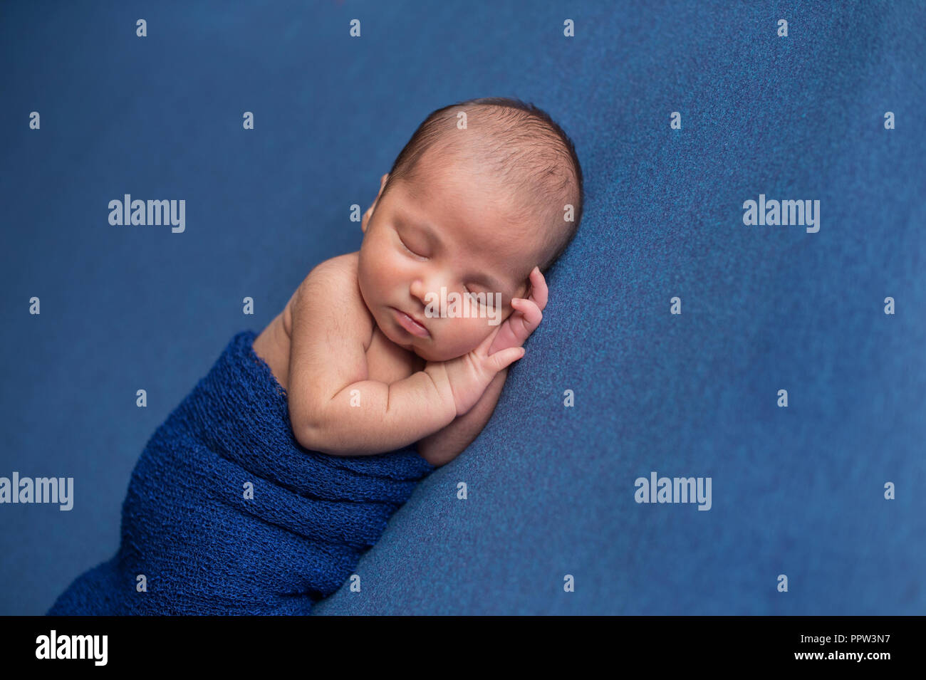 Sleeping, nine day old newborn baby boy swaddled in a blue wrap. Shot in the studio on denim blue material. Stock Photo