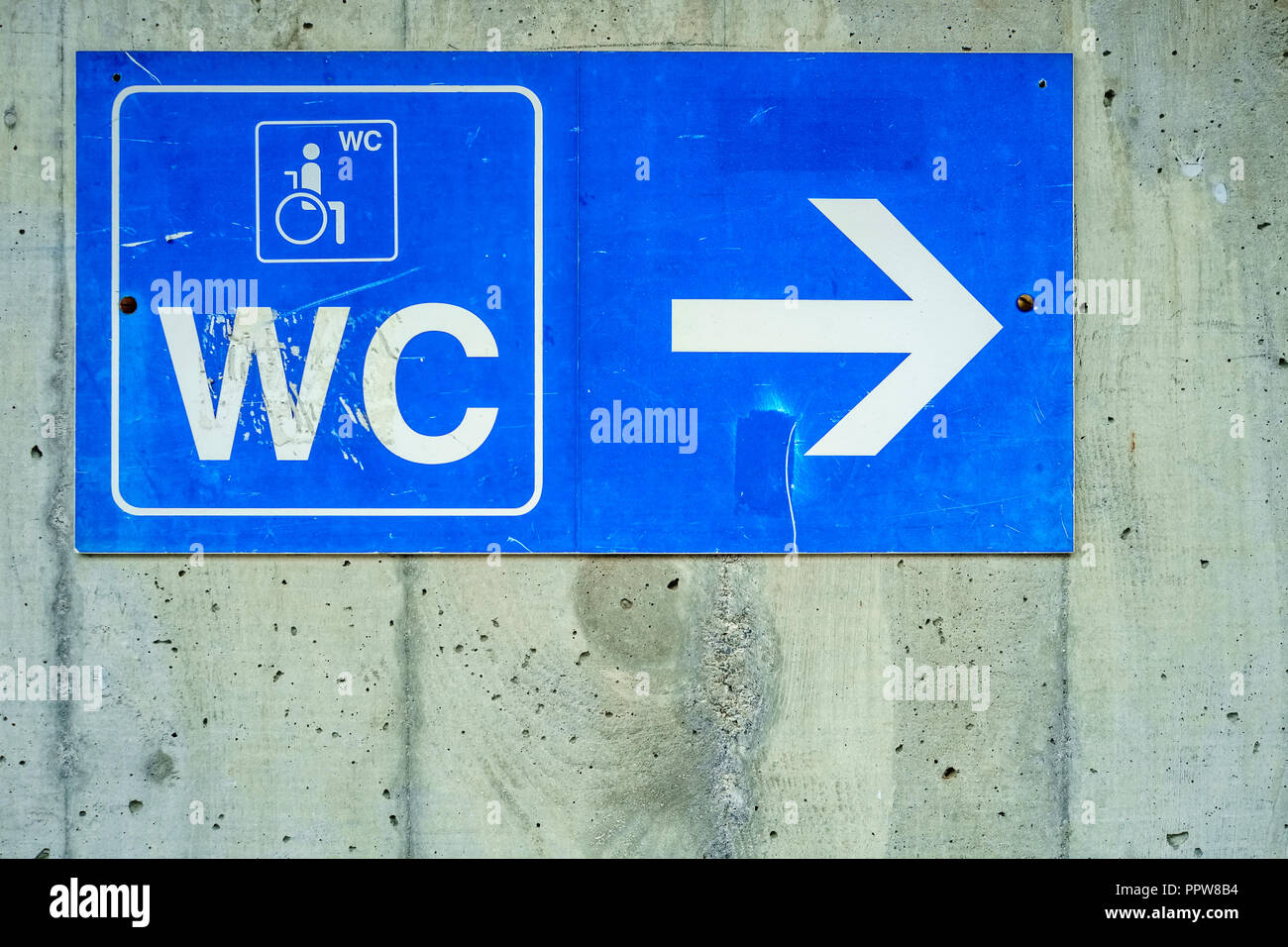 A blue sign against a concrete wall is indicating where the restroom is at the railway station of the Swiss village of Wengen (Berner Oberland). Stock Photo