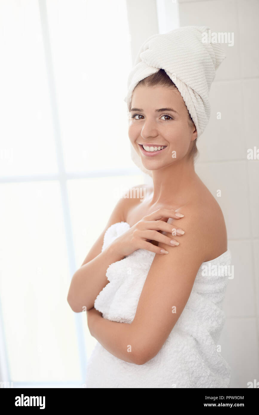Pretty healthy young woman wrapped in white towels standing in a bathroom with eyes closed and a happy smile in a spa treatment, wellness and personal Stock Photo