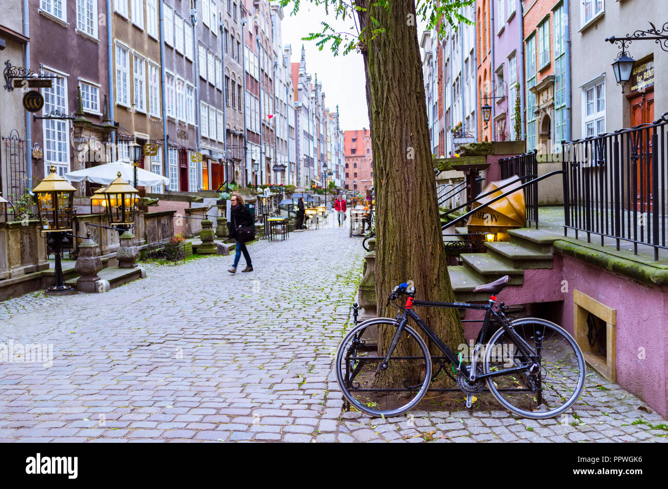 Gdansk, Pomerania, Poland : A bicycle leans on a tree as people walks at St. Mary's Street (ul. Mariacka) in the heart of the old town. Stock Photo