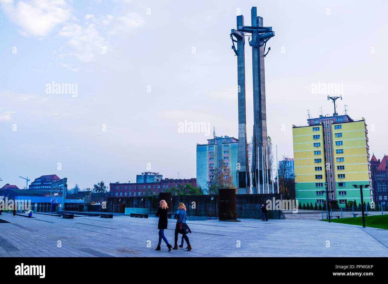 Gdansk, Pomerania, Poland : Two women walk past the Monument to the Fallen Shipyard Workers of 1970 at Solidarity Square (Plac Solidarności) Designed  Stock Photo