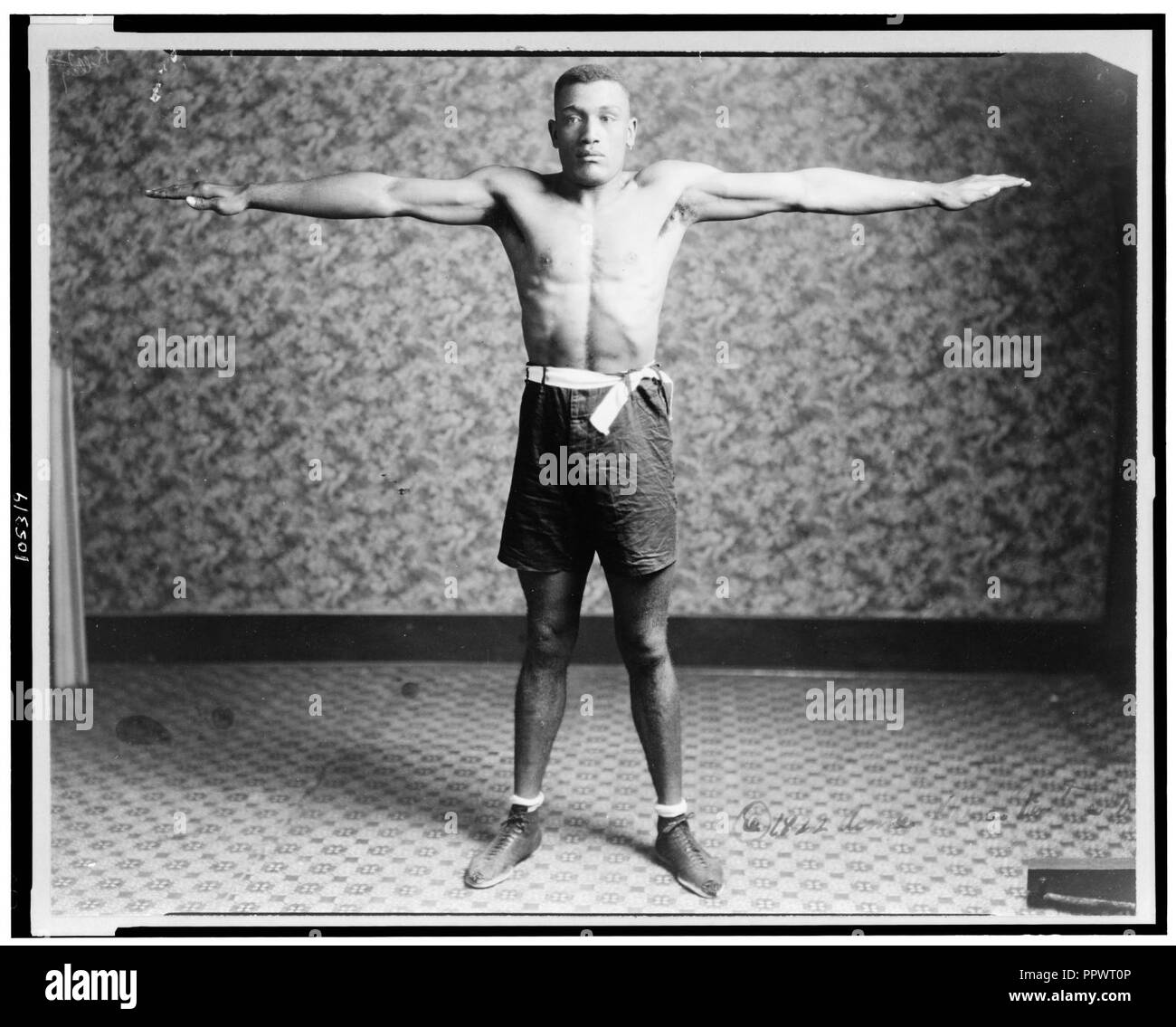 Boxer Tut Jackson clothed in boxing trunks, full-length portrait, standing, facing front, with his arms extended out from his sides, showing his reach Stock Photo