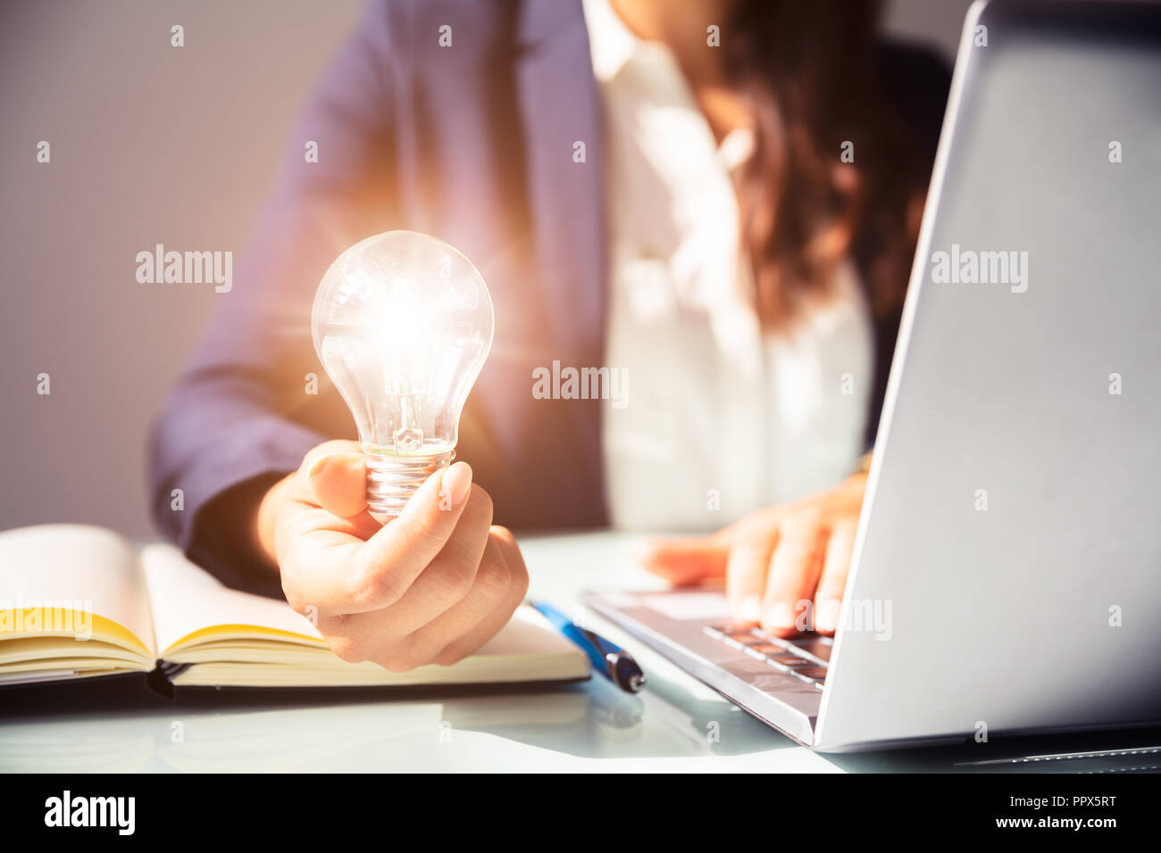 Close-up Of A Businesswoman's Hand Holding Illuminated Light Bulb In Office Stock Photo