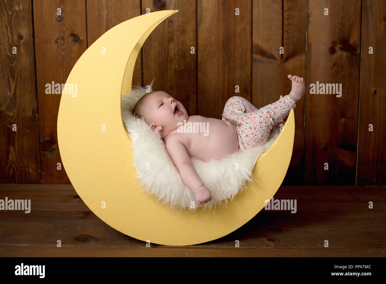 Studio portrait of a yawning, one month old baby girl lying on a moon shaped posing prop. Stock Photo