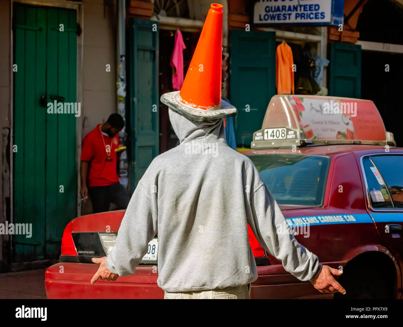 A man wearing a traffic cone as a hat tries unsuccessfully to hail a cab in the French Quarter, Nov. 15, 2015, in New Orleans, Louisiana. Stock Photo