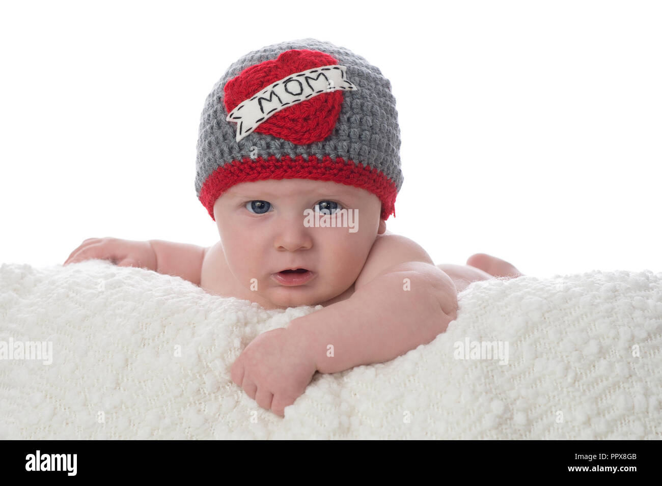 A 2 month old baby boy lying on his stomach on a white blanket. He is wearing a crocheted hat that says, 'Mom' on it. Shot in the studio on a white ba Stock Photo
