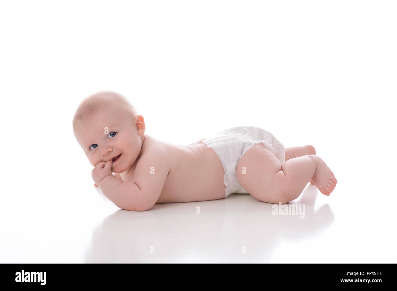 A 2 month old baby boy lying on his stomach on a white, seamless background. He is wearing a plain, white diaper and has his fingers in his mouth. He  Stock Photo