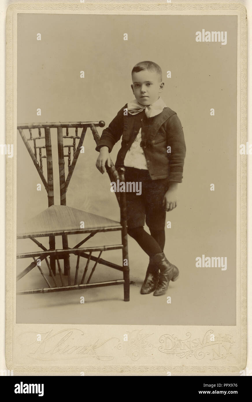 Young boy, standing, posed at angular chair; F.J. Klink, American, active 1890s, about 1890; Gelatin silver print Stock Photo