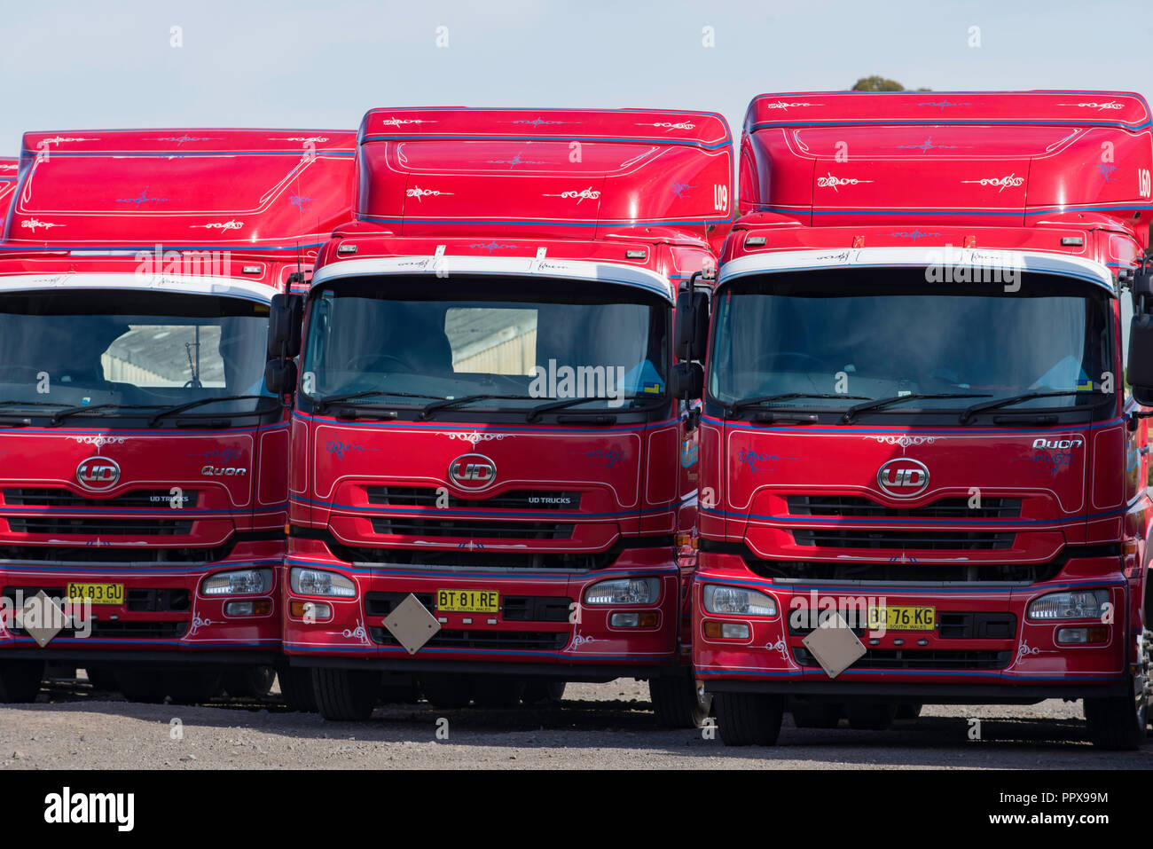 Three red UD prime mover trucks parked side by side with drag reducing fairings and white sun visors to reduce glare from the Australian sun Stock Photo