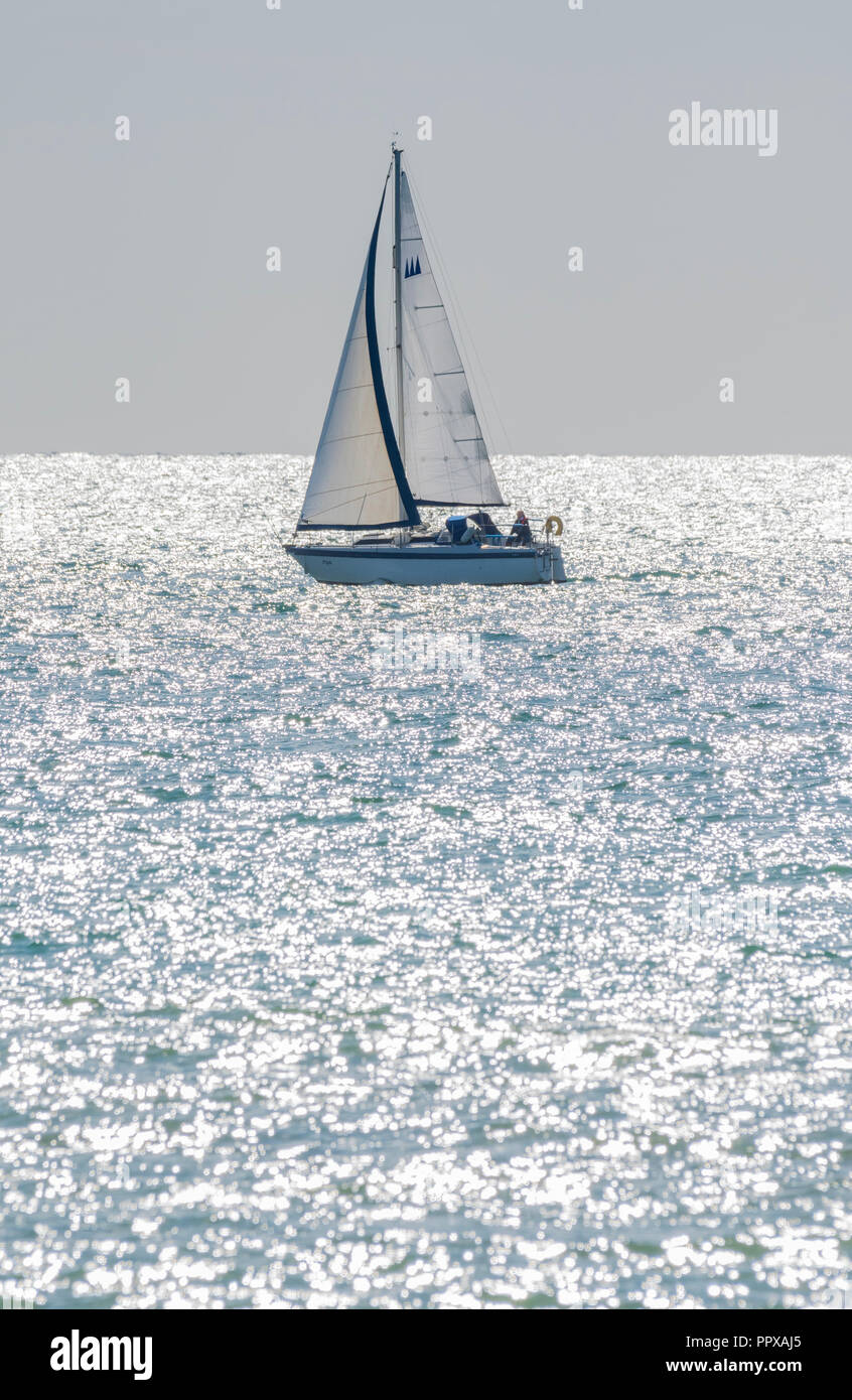 Single person yacht sailing at sea with the morning sun sparkling in the ocean, in the UK. Stock Photo