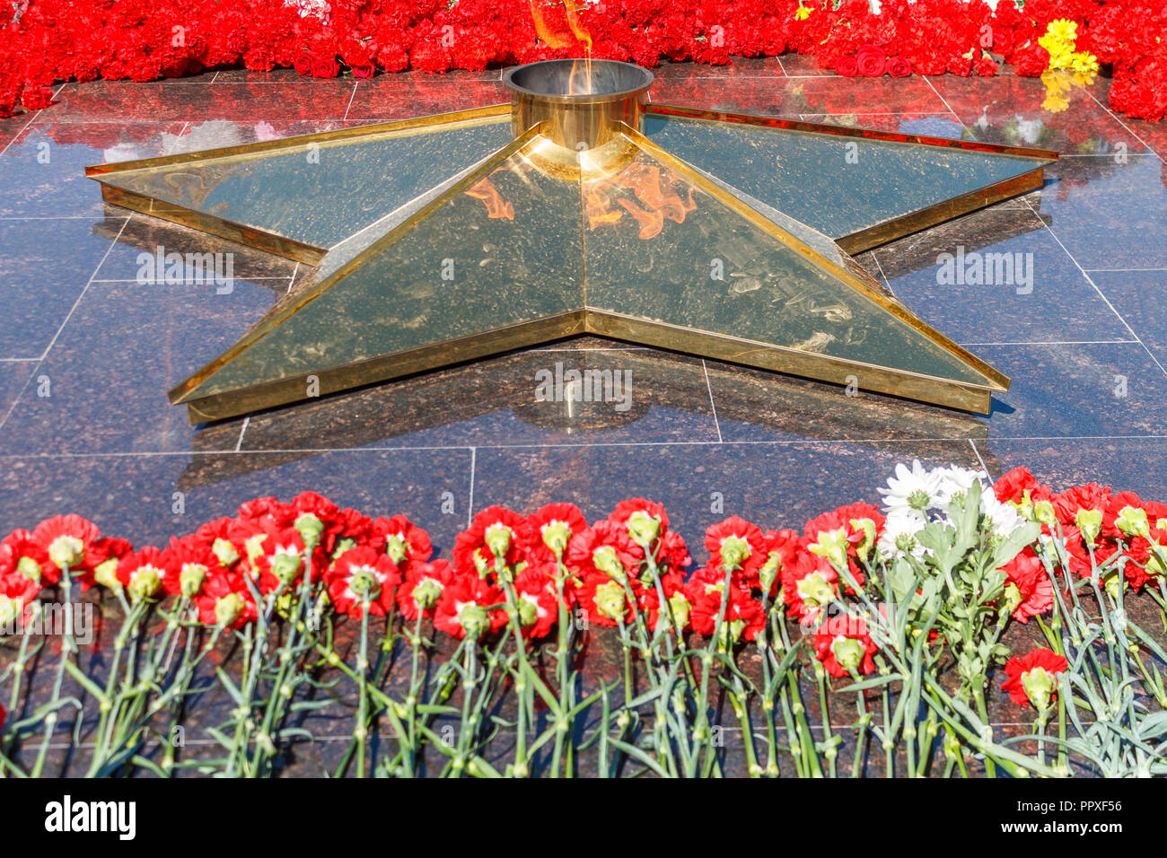 Many red flowers lie on a black granite monument with a star from which ...