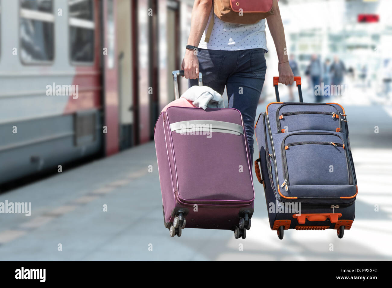 A girl from the back with two suitcases on a blurred background of a railroad train and train. Stock Photo