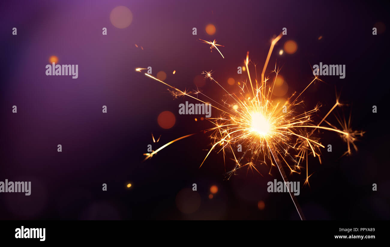 Glittering burning sparkler on purple background Stock Photo