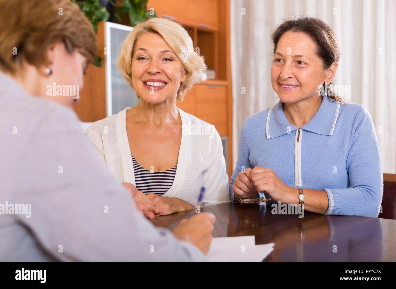 Senior ladies signing documents at bank with agent. Focus on blonde Stock Photo