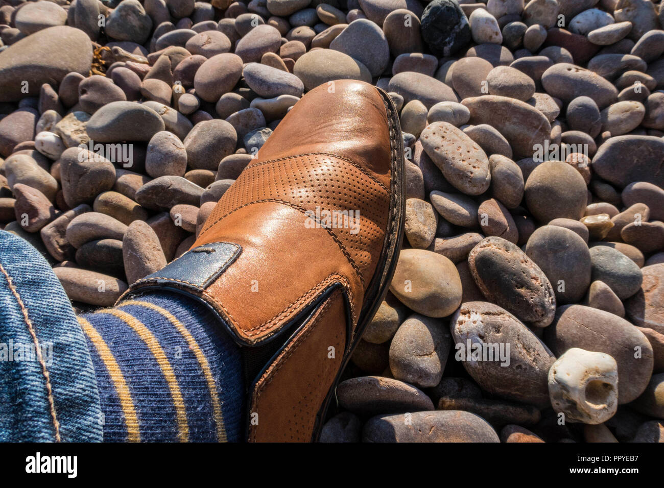 A tan shoe walking on colourful pebbles on Sidmouth beach. Stock Photo