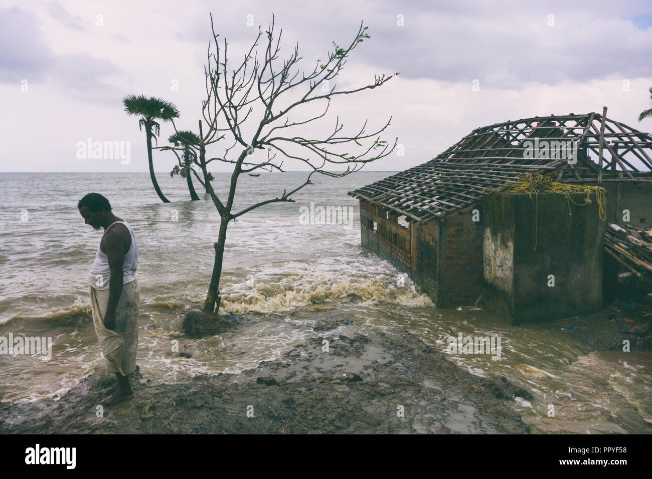 Akhter stands near his lost home in Mousuni Island at Gangetic delta region, which he had to abandon a ween before. Few weeks later he left the island to work in Kerala in South India. There too, he had to leave due to heavy flooding in recent times during the monsoon of 2018. Stock Photo