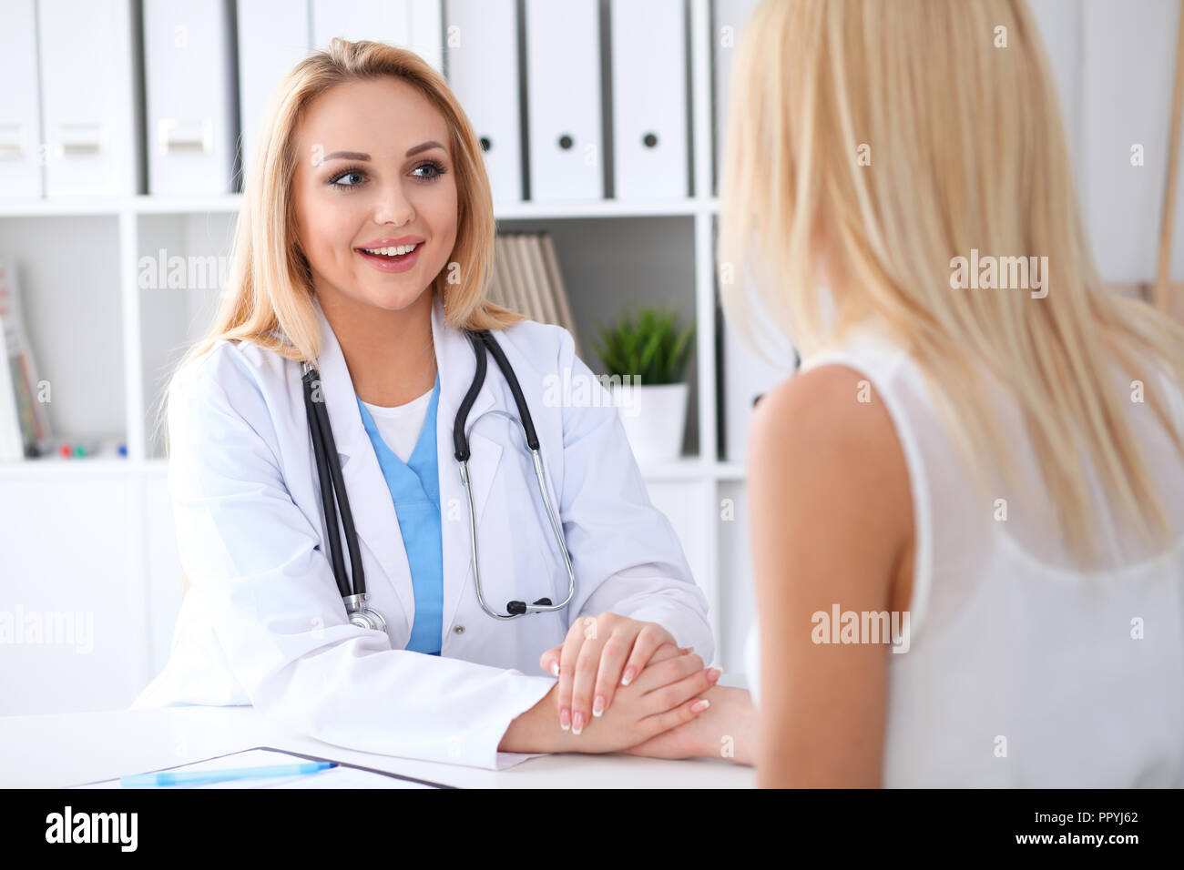 Doctor woman reassuring her female patient while holding hands ...