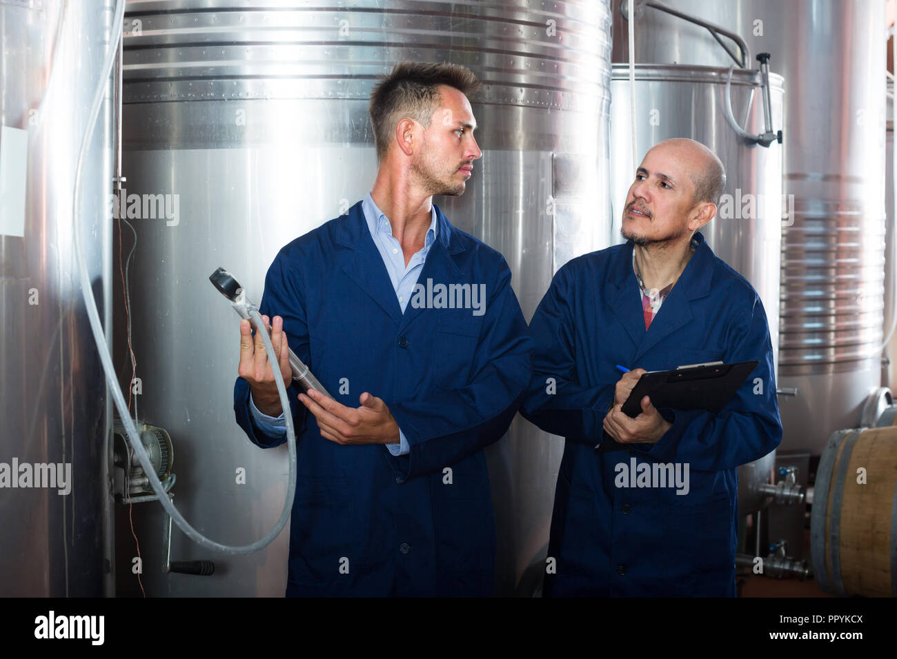 Two winery workers  in uniform working and taking notes in secondary fermentation section Stock Photo