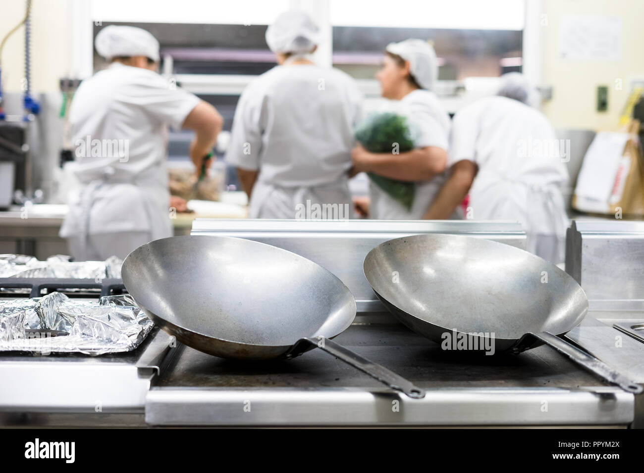 Two silver big frying pans with four kitchen workers wearing aprons as a background Stock Photo