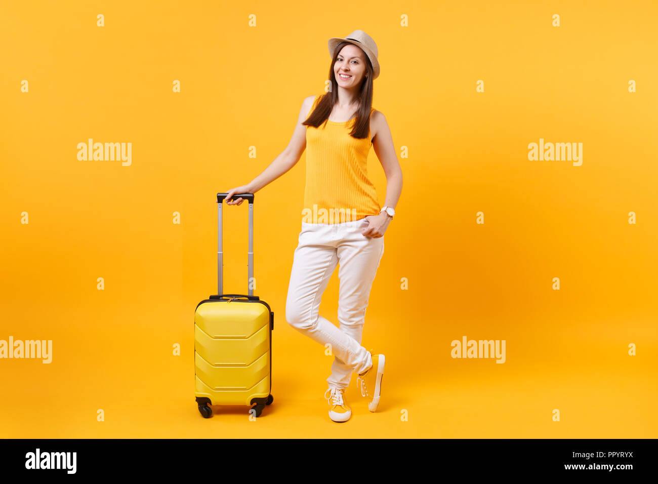 Traveler tourist woman in summer casual clothes, hat with suitcase isolated on yellow orange background. Female passenger traveling abroad to travel o Stock Photo