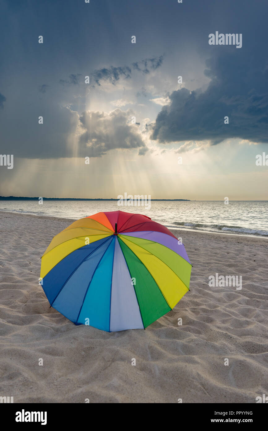 Multicolored umbrella on the beach against dramatic stormy clouds Stock Photo