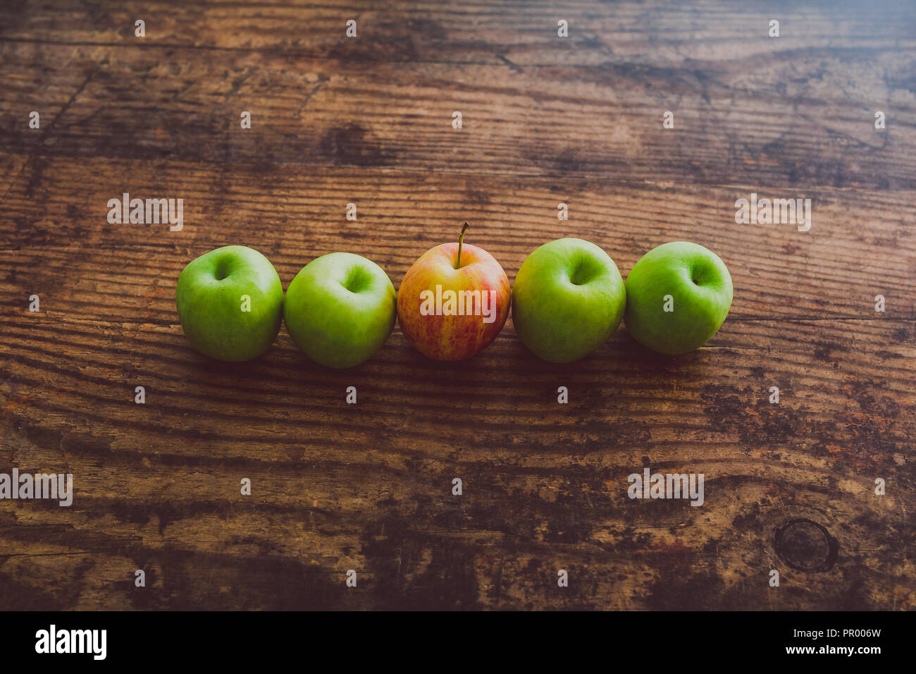 one single red apple among other green ones on wooden table, concept of one single red apple among other green ones on wooden table, concept of