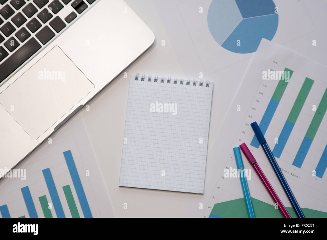 Office table with blank notepad and laptop. Work papers with diagrams ...