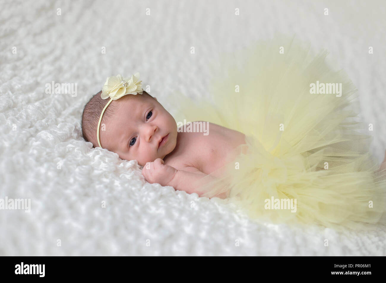An alert, 2 week old newborn baby girl wearing a yellow headband and tutu. Stock Photo