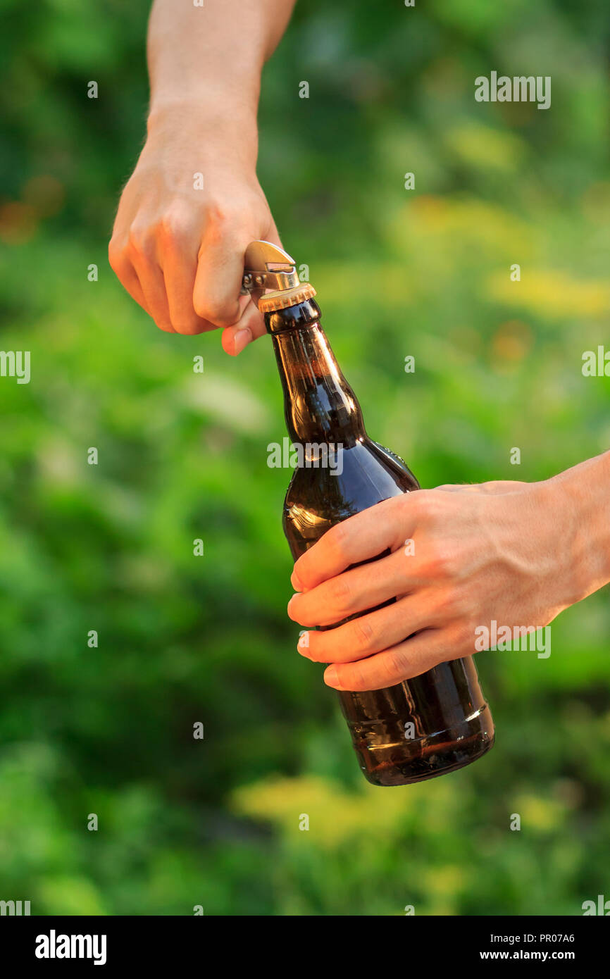 Young man is opening bottle of beer with old opener on natural blurred background Stock Photo