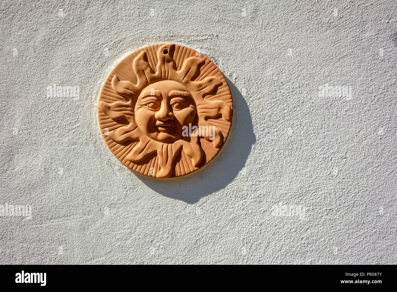 Looking at a round, hand-made clay art object depicting the sun. It hangs on a white stone wall in the Swiss village of Lauterbrunnen (Bernese Alps) Stock Photo