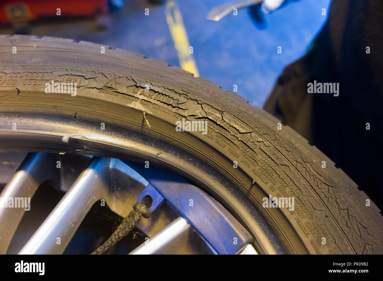 Tyre fitter / mechanic remove / removing / removes / removal of cracked  old tire with crack / cracks on side wall sidewall & car / cars wheel rim. UK Stock Photo
