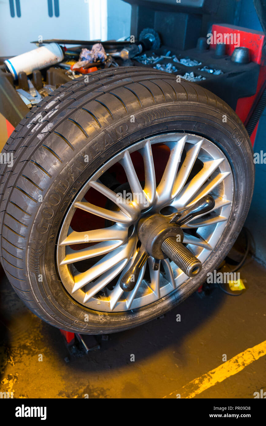 A car rim fitted with a new tyre / tire on a wheel balancing machine shown with a tray of