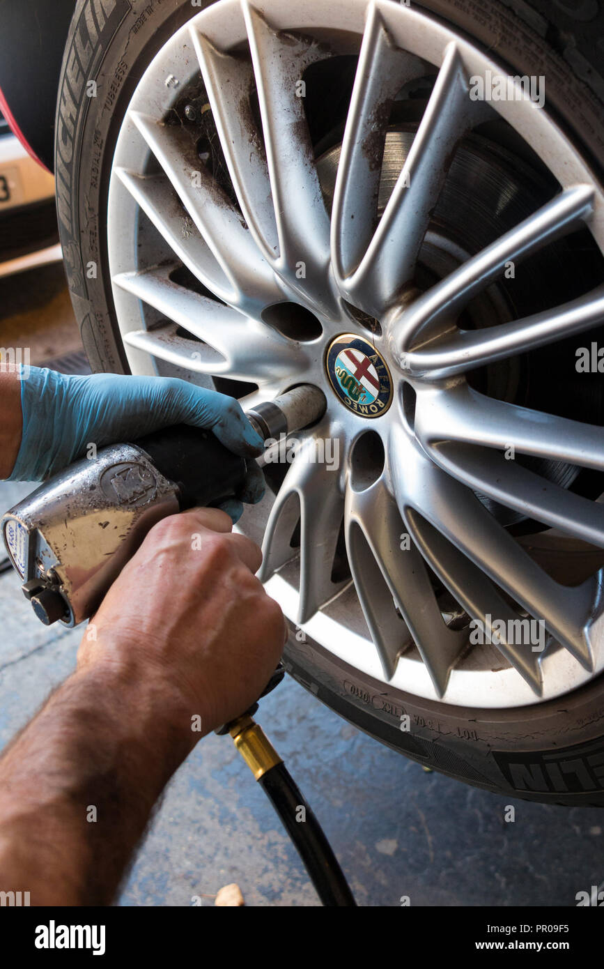 Tyre fitter / mechanic loosening / unscrewing / loosens bolts on a car wheel with an old perished tyre so it can be changed for a new tyre. (102) Stock Photo
