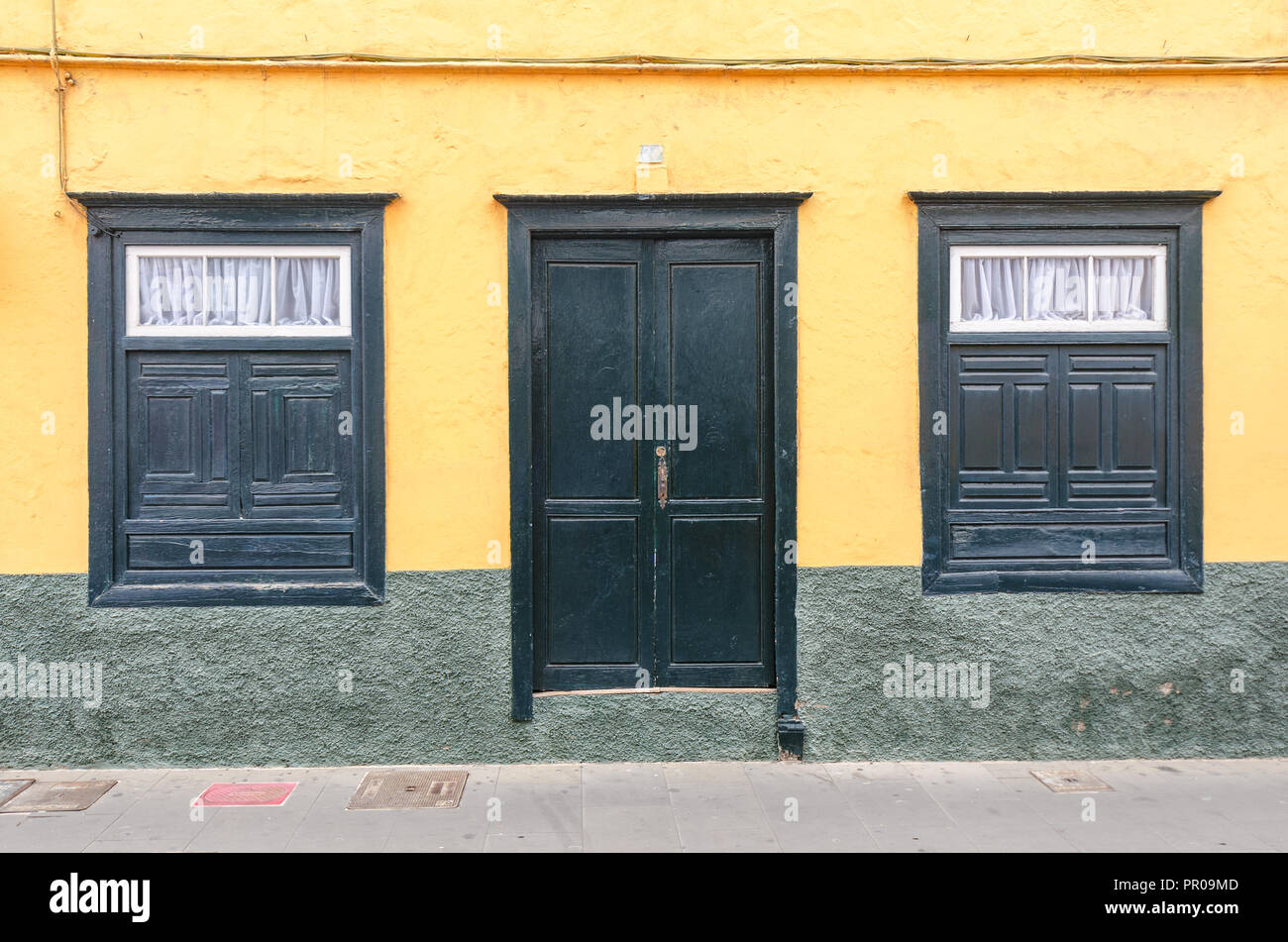 Green Door And Two Windows On A Yellow Facade Of An Old House