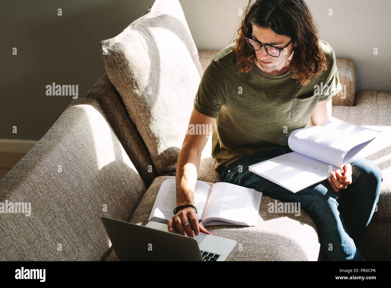 Male student looking at a laptop while studying. Student preparing for college exams sitting at home. Stock Photo