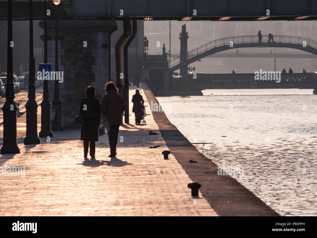 Paris Canal St. Martin - people strolling along the waterfront in the late afternoon sun, bridges in distance Stock Photo