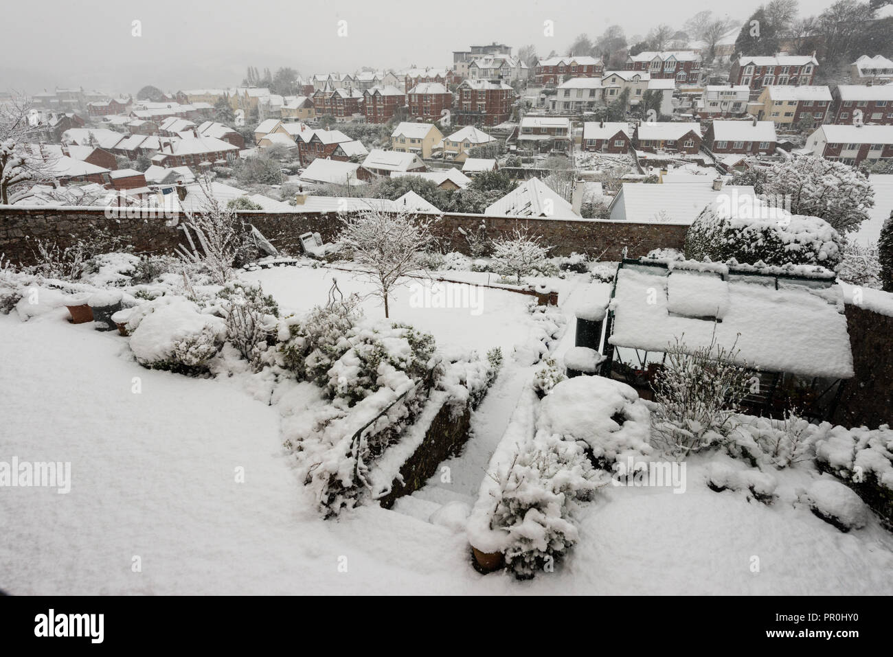 Snow over a garden and surrounding town buildings and their rooftops. Stock Photo