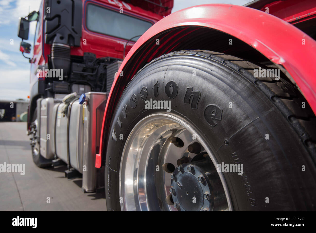 A close up image of a shiny black painted tyre, tire of a large red prime mover truck parked and stationary Stock Photo
