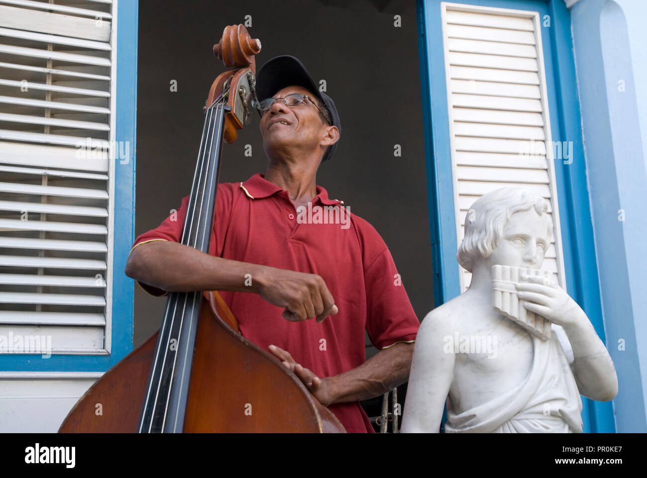 Cello musician resting on his instrument next to a classic sculpture of a flute player  in Cuba Northern Caribbean Stock Photo