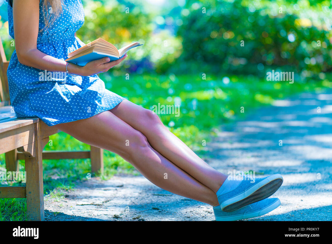 Woman in a blue dress sitting on a bench in a city park and reading a ...