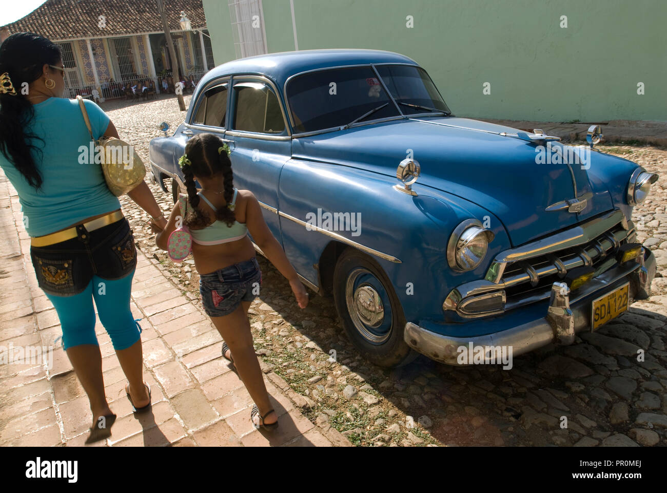 Mother and daughter walking by a blue vintage American car in the streets of Trinidad Cuba West Indies Stock Photo