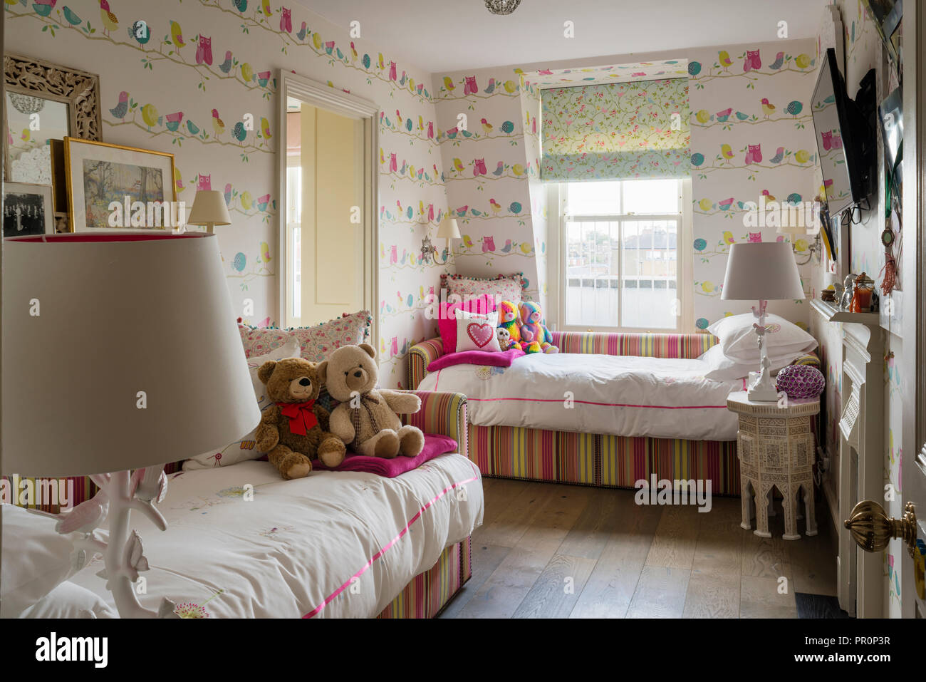 Striped daybeds with bird patterned wallpaper in girls room Stock Photo